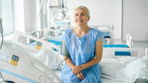 Female patient sitting on hospital bed in blue medical gown smiling