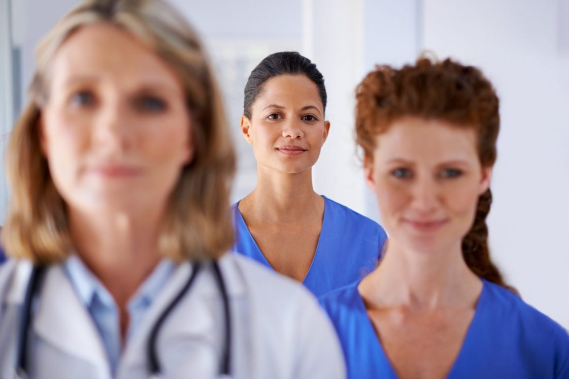 Blurred endometriosis specialist and nurse in foreground with in-focus nurse centred between them in the background.
