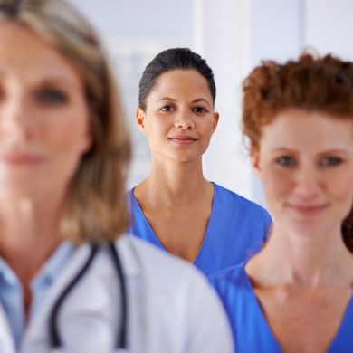 Blurred endometriosis specialist and nurse in foreground with in-focus nurse centred between them in the background.
