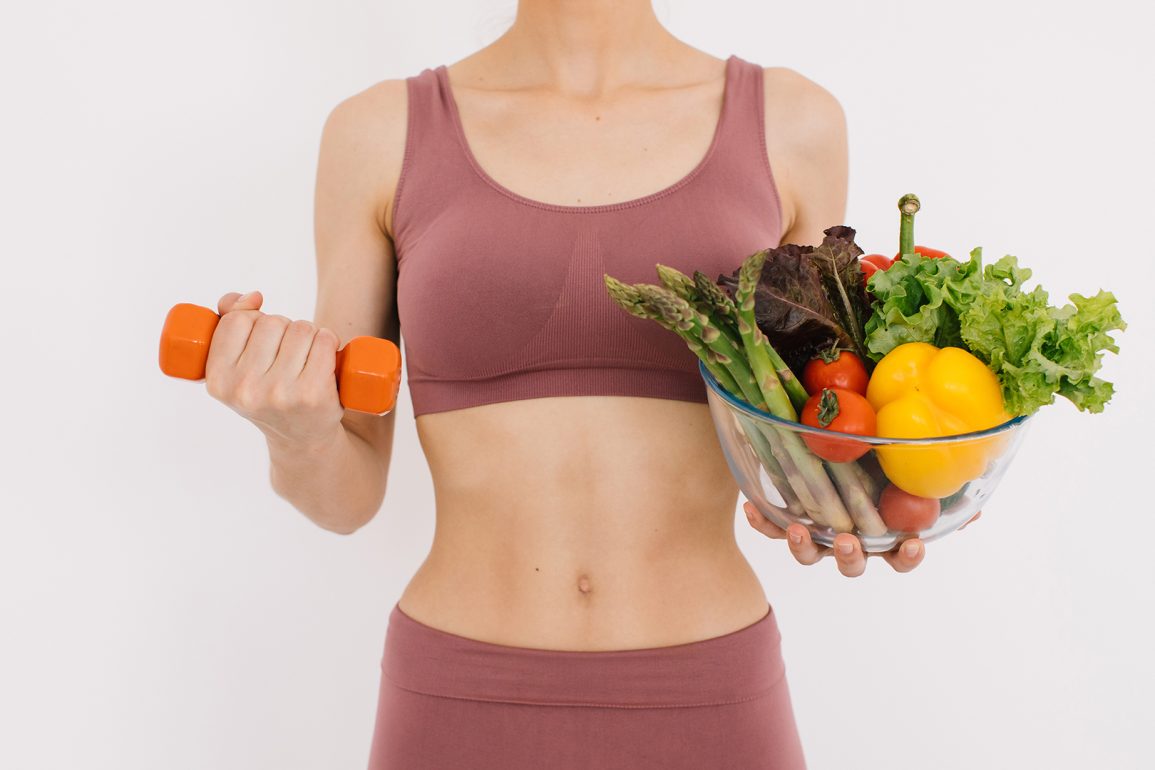 A young woman in exercise clothing holds a dumbbell and salad