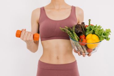 A young woman in exercise clothing holds a dumbbell and salad