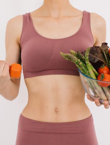 A young woman in exercise clothing holds a dumbbell and salad