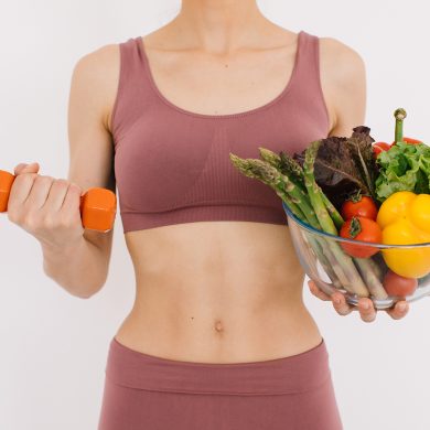 A young woman in exercise clothing holds a dumbbell and salad