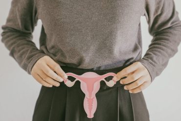 A woman holds up a paper cutout of a uterus, fallopian tubes, and ovaries