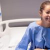What to Expect Before, During, and After Laparoscopy Surgery for Endometriosis 25 Woman in a blue hospital gown smiling from a hospital bed