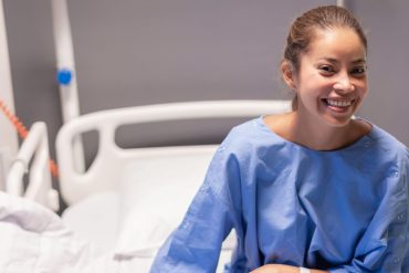What to Expect Before, During, and After Laparoscopy Surgery for Endometriosis 20 Woman in a blue hospital gown smiling from a hospital bed