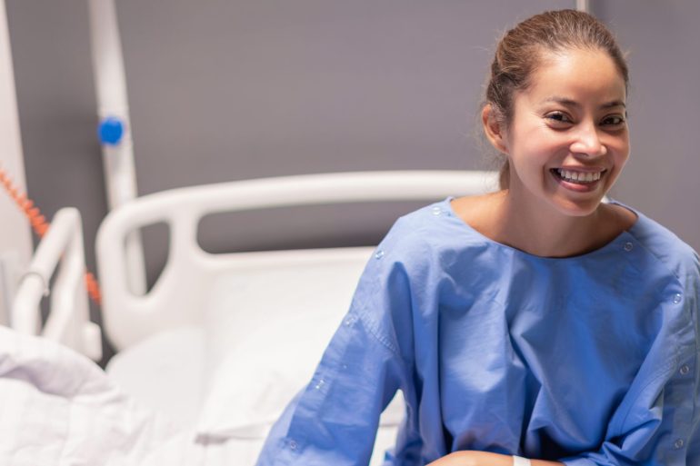 Woman in a blue hospital gown smiling from a hospital bed